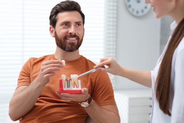 dentist shows patient a plastic diagram of dental implants